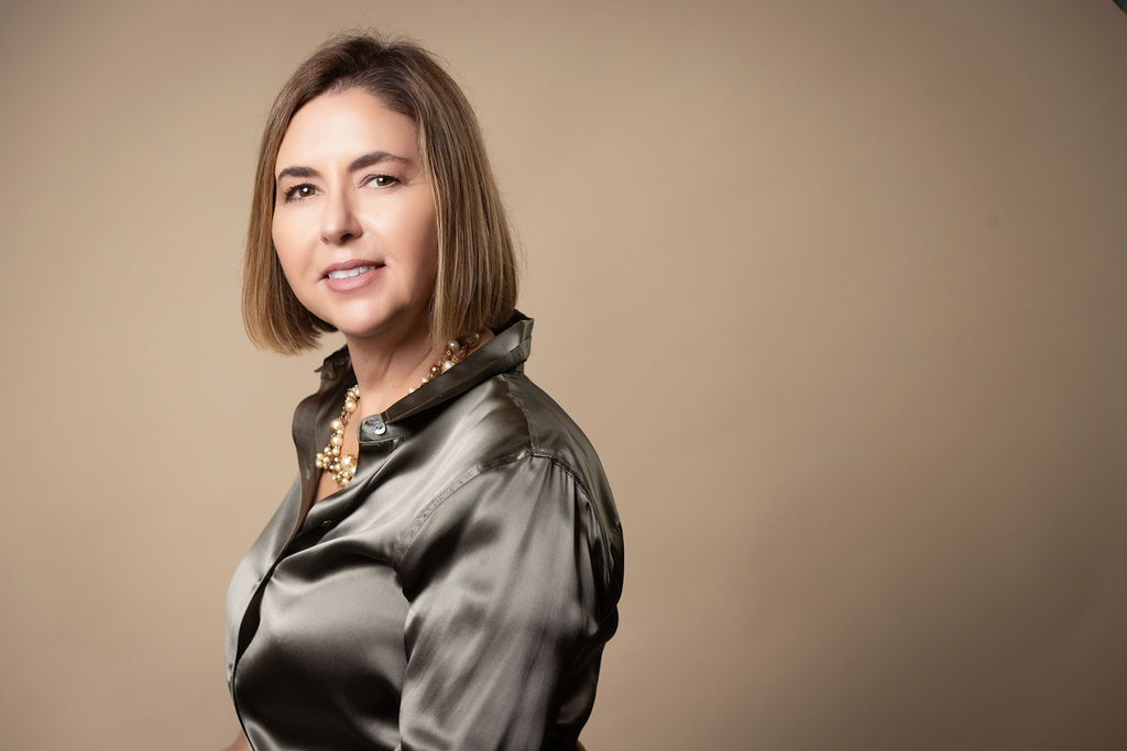 Ingrid Rainey, Managing Partner of Rainey Law P.C., wearing a dark satin blouse against a warm taupe backdrop